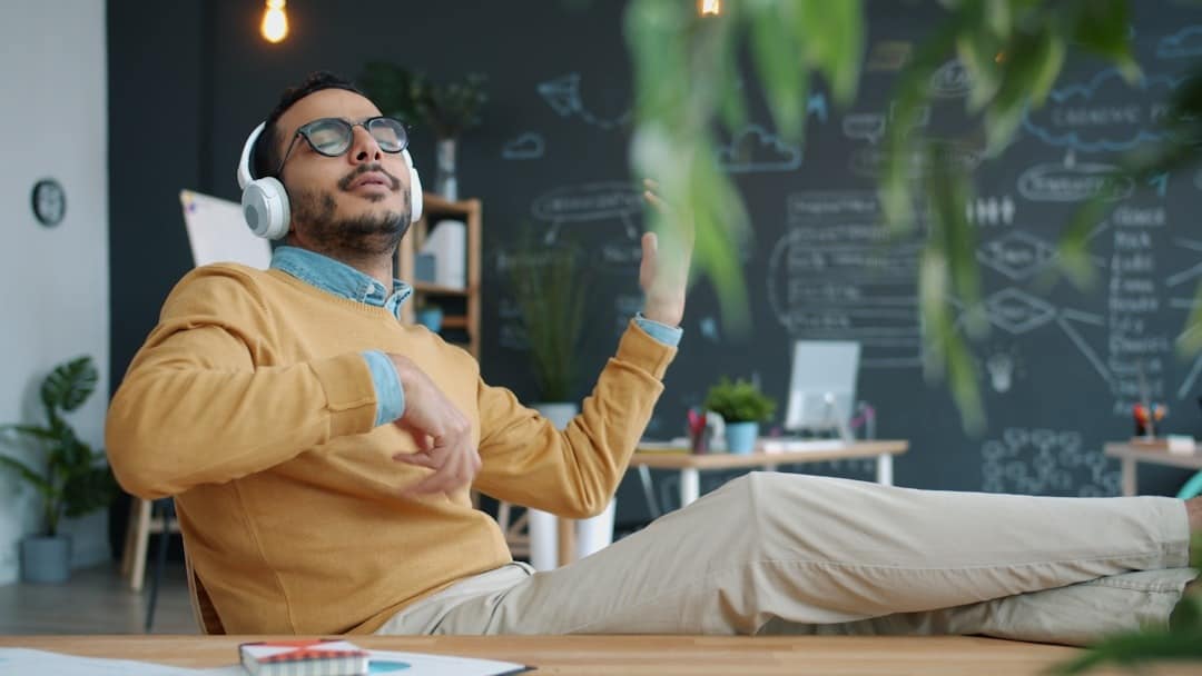 Man in headphones playing air guitar in office.
